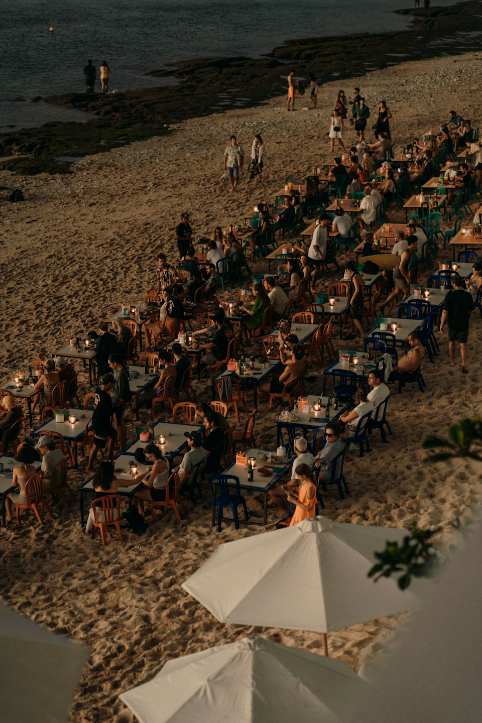 Ludzie jedzący posiłki przy stolikach na plaży nad oceanem.